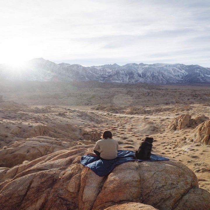A person and their dog using the blanket on a large rock in the desert 