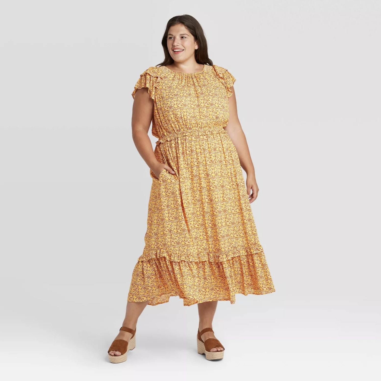 Model is wearing a yellow floral short sleeve dress with a ruffled hem and brown wedges
