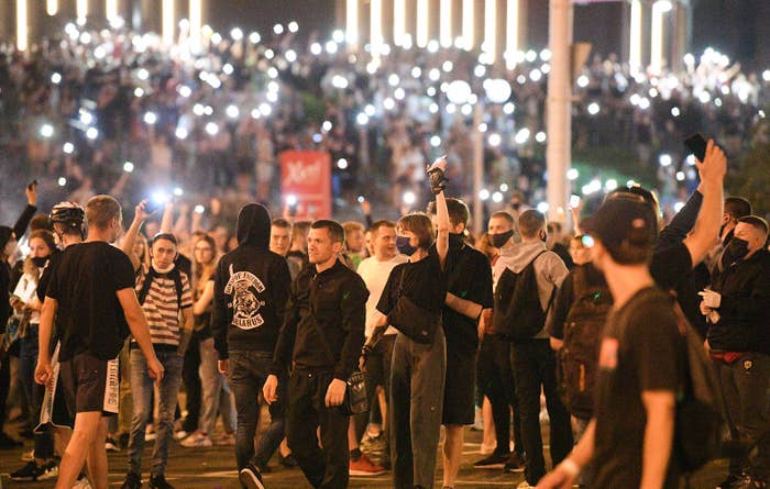 A large crowd gathered, hold their hands over their heads, using their phones as lights