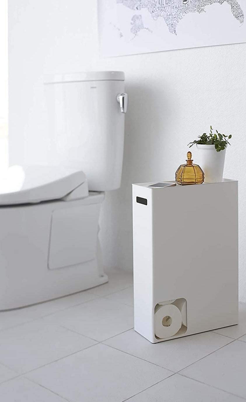 White rectangle holder with a small square cut out in the bottom left corner, revealing rolls of toilet paper inside