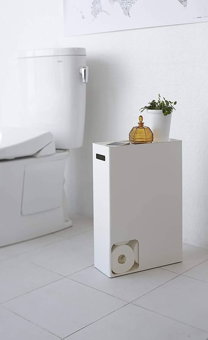 White rectangle holder with a small square cut out in the bottom left corner, revealing rolls of toilet paper inside