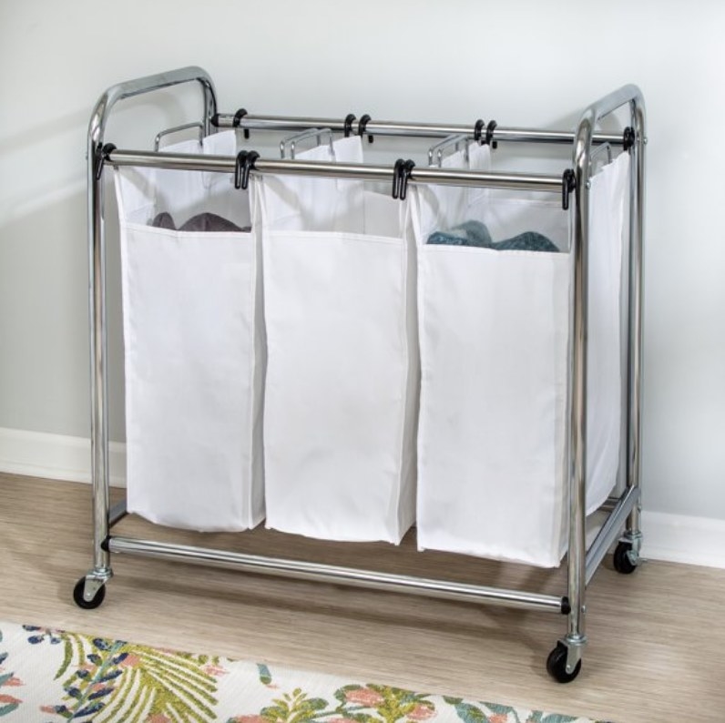 A metal frame with four caster wheels holding three white cloth laundry bins