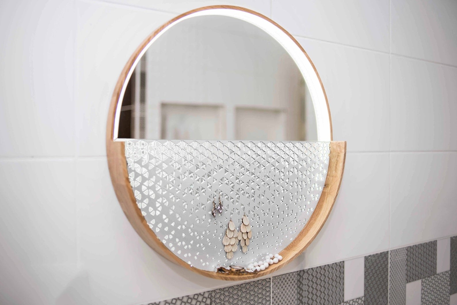 A round mirror with wood frame, lights in between the mirror and frame and a white holder on the bottom half with earrings hanging from it