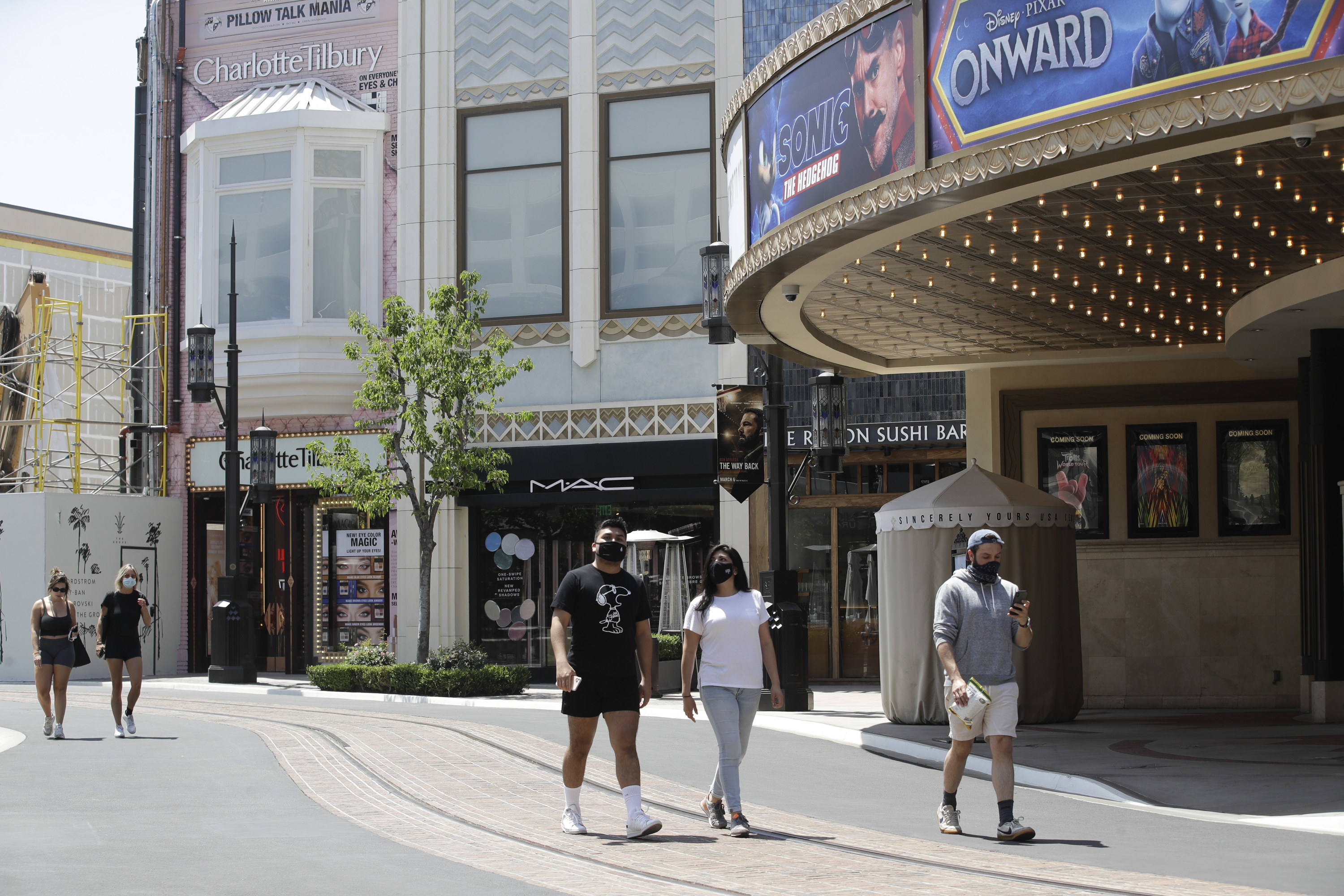 Five people, most wearing masks, walk down an otherwise empty outdoor street at the Grove outdoor mall