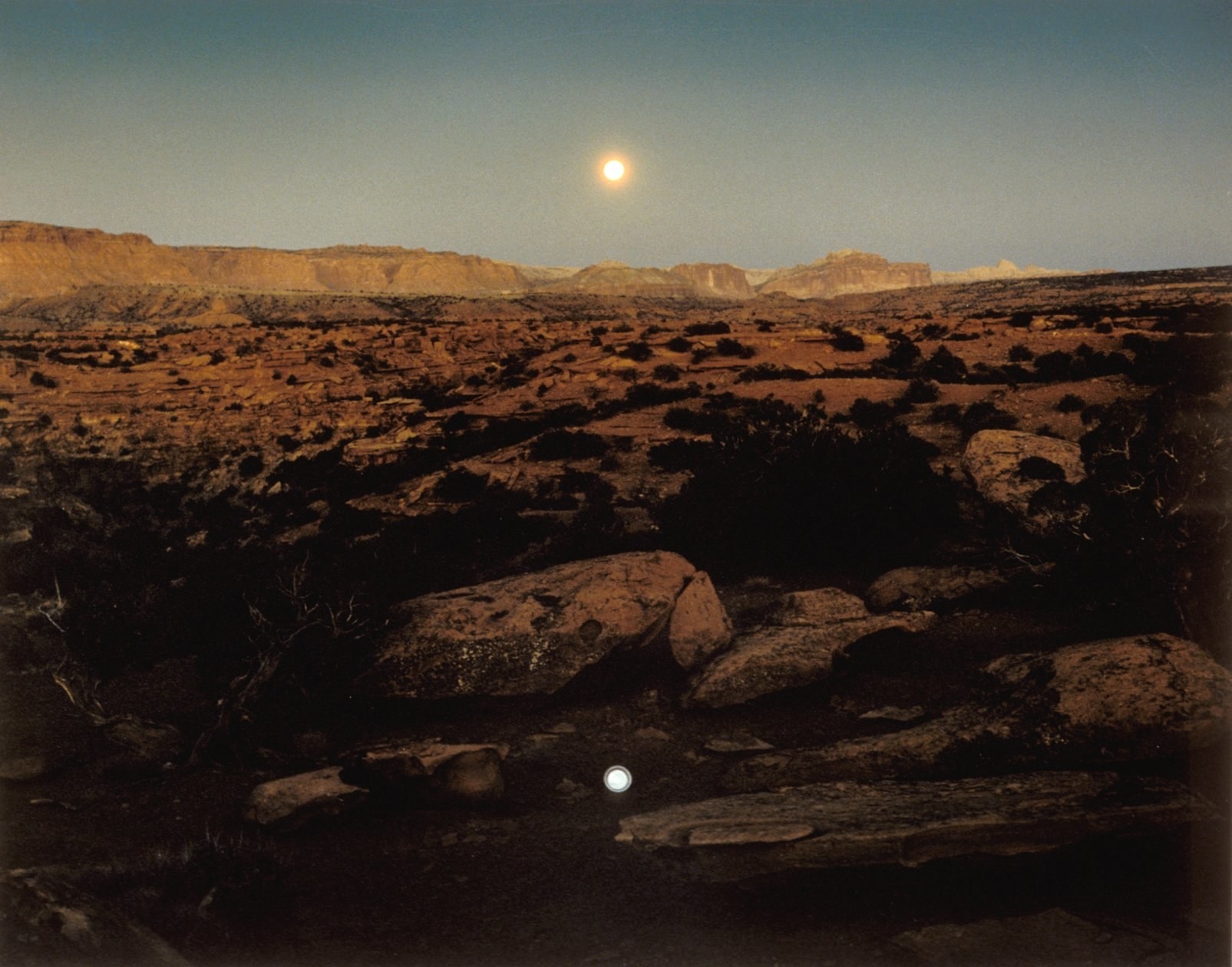 Out in the desert, a moon rises over a pie plate that also looks like a moon