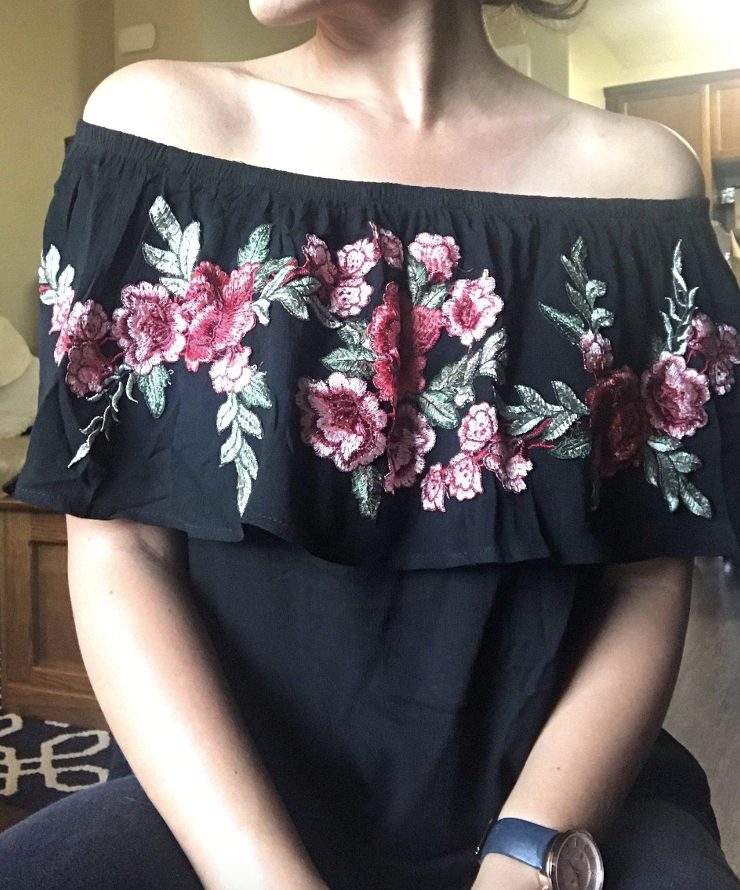 reviewer wearing black off-shoulder ruffle top with embroidered florals