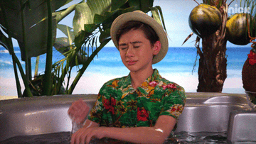 Gif of someone in a jacuzzi somewhere tropical, decked out in bermuda hat and Hawaiian shit, and wiping away tears