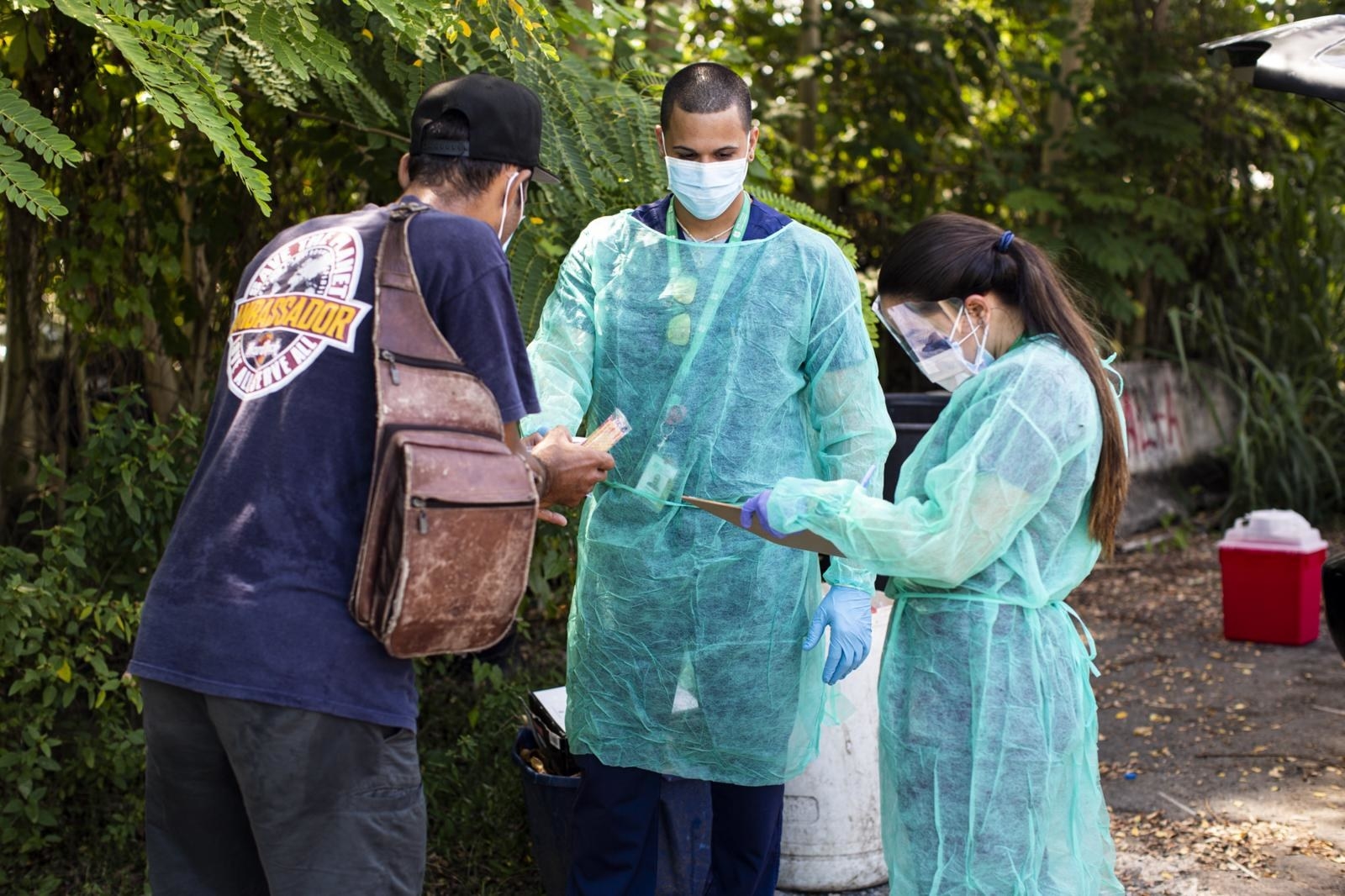 Two people wearing PPE talk to another man