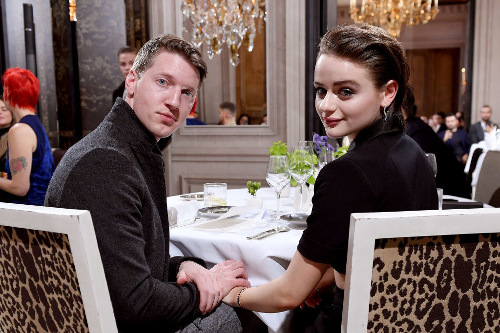 Joey King and Steven Piet holding hands and turning to pose for a photo while seated at a table 