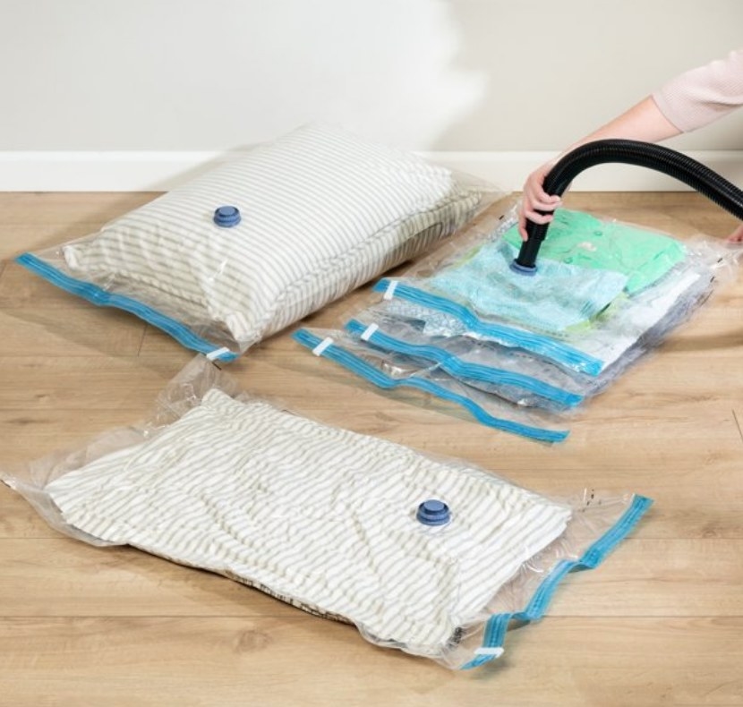 A model&#x27;s hand vacuuming air from clear storage bags filled with clothes and pillows