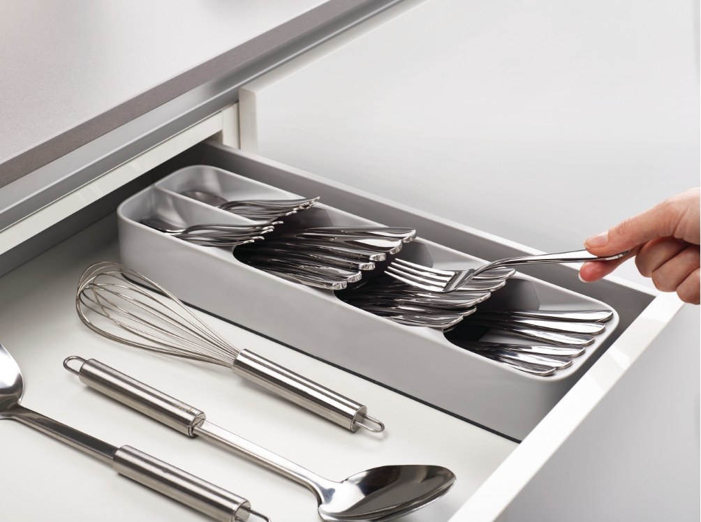 A model&#x27;s hand placing silver cutlery into a white plastic organizer