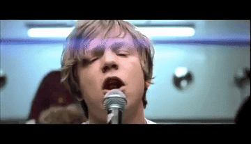 A GIF of the lead singer of Cage the Elephant singing and the staring at a woman in straight jacket who disappears.