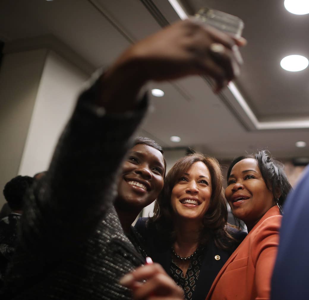 Three Black women look at a camera phone and smile