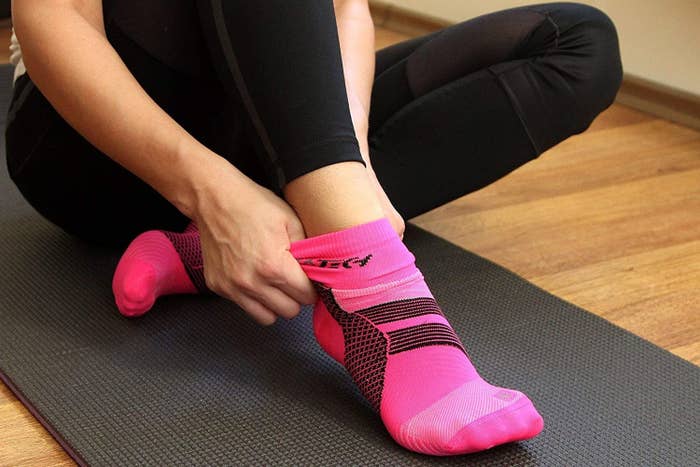 A person sitting on a yoga mat pulling on the compression socks