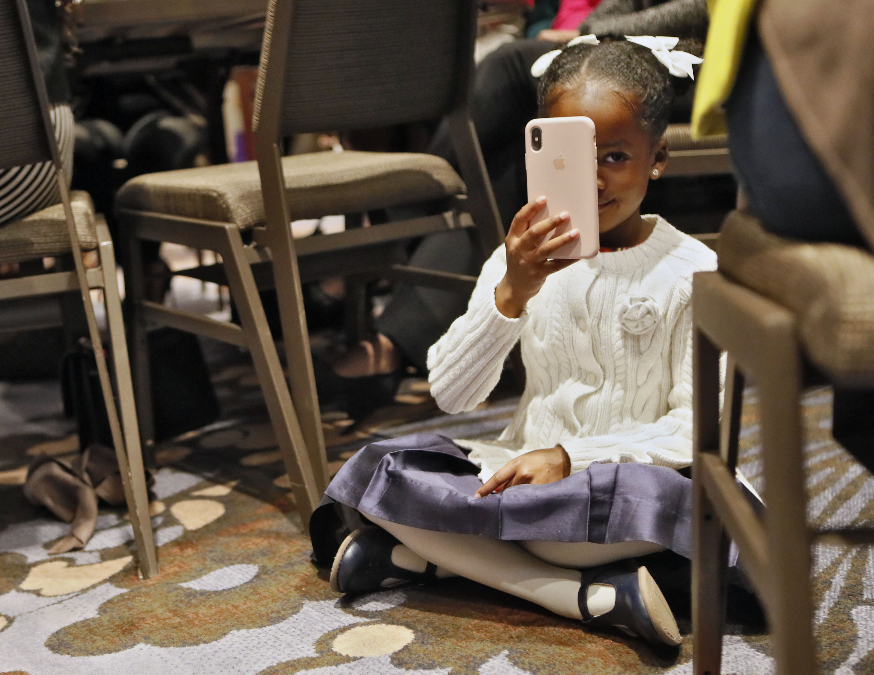 A young black girl sits on the floor and holds up a phone to take a picture