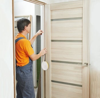 Product photo showing a person applying Weather Stripping to a door frame by simply sticking and rolling it along the edge of the frame, preventing drafts and increasing energy efficiency