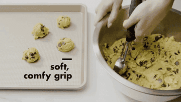 A GIF of someone scooping cookie dough out of a bowl with a large spoon and placing the dough on a baking pan