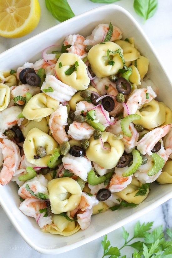 A bowl of chopped shrimp, cheese-filled tortellini, celery, olives, and capers.