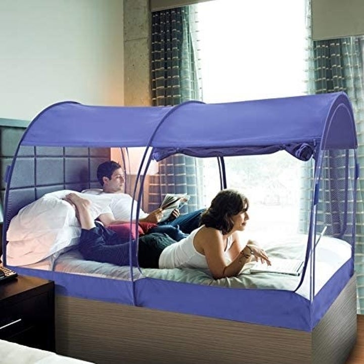 A side view of the bed tent on a mattress with the privacy panels lifted up to show two people in it 