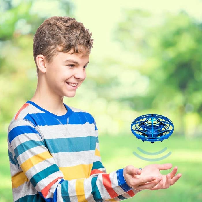 A kid with the blue mini drone hovering above their hands 