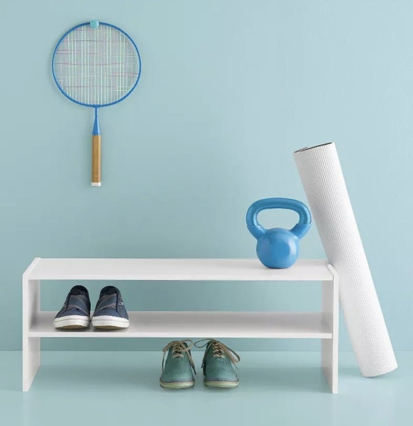 A white, wooden unit with two shelves and no bottom holding two pairs of shoes and a kettleball