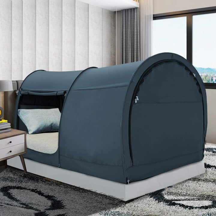A black tent over a twin mattress with a side door zippered open 