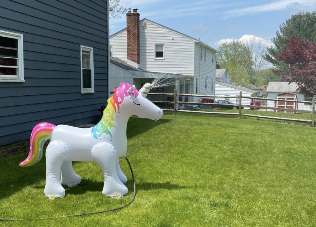 reviewer image of the inflatable unicorn sprinkler with water shooting out of its horn in a backyard