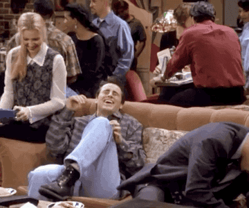 The cast of Friends laugh on a couch at their favorite coffee shop