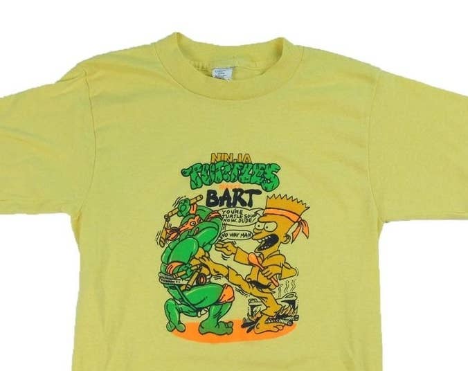 A yellow bootleg Simpsons T-shirt that features Bart in a karate outfit beating up a Teenage Mutant Ninja Turtle.