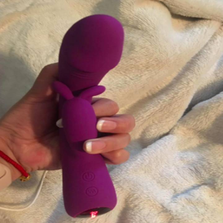 Reviewer holds purple waterproof vibrator in their hand on top of a soft white blanket