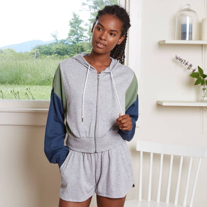 model wearing gray drawstring zip-up hoodie with green and blue sleeves