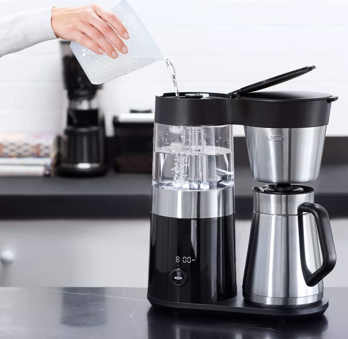 Model&#x27;s hand pouring water into a black and silver OXO coffee maker