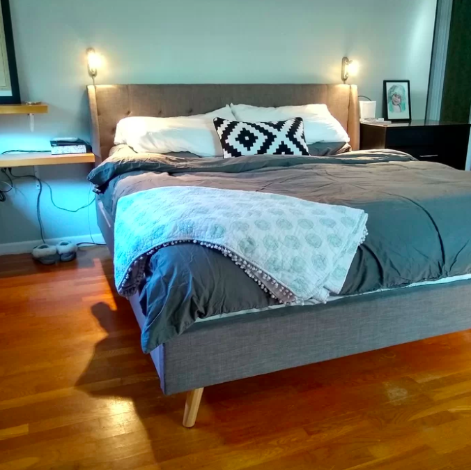 Reviewer&#x27;s gray platform bed covered in a gray duvet cover with a patterned pillow and circle blanket