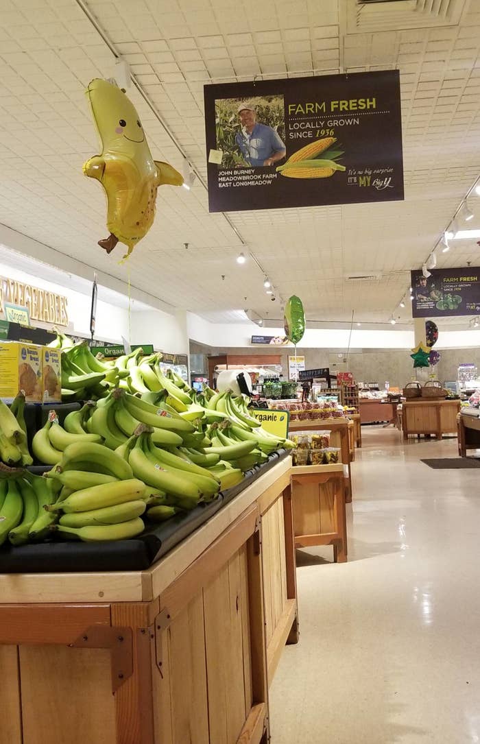 A produce section of a grocery store with a banana balloon above the bananas.