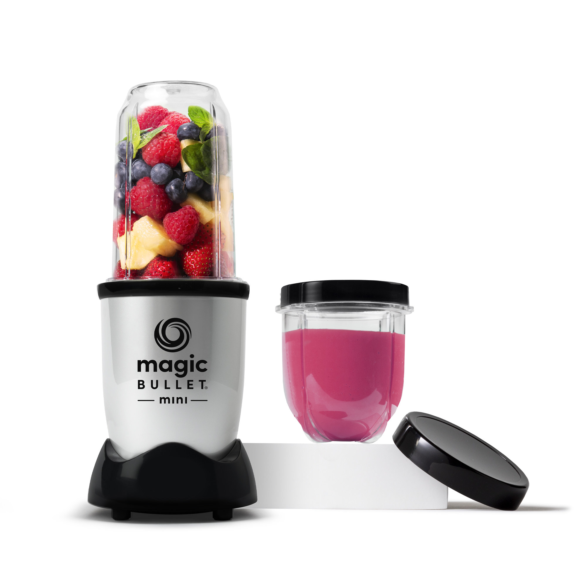 A silver blender with a black base and clear plastic cup filled with fruit next to a smoothie