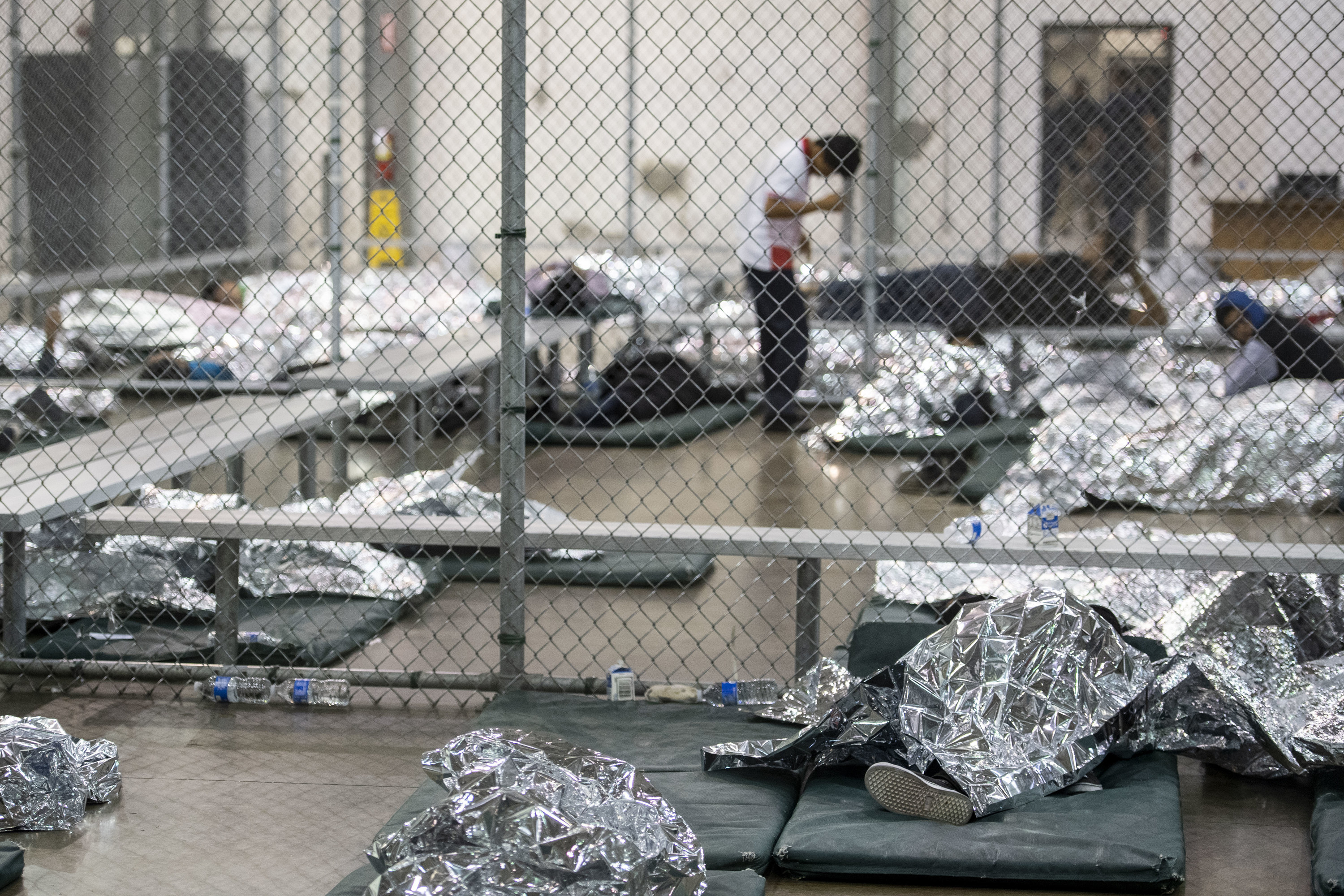 The children lie on padded mats on the floor, in groups separated by wire fencing.  