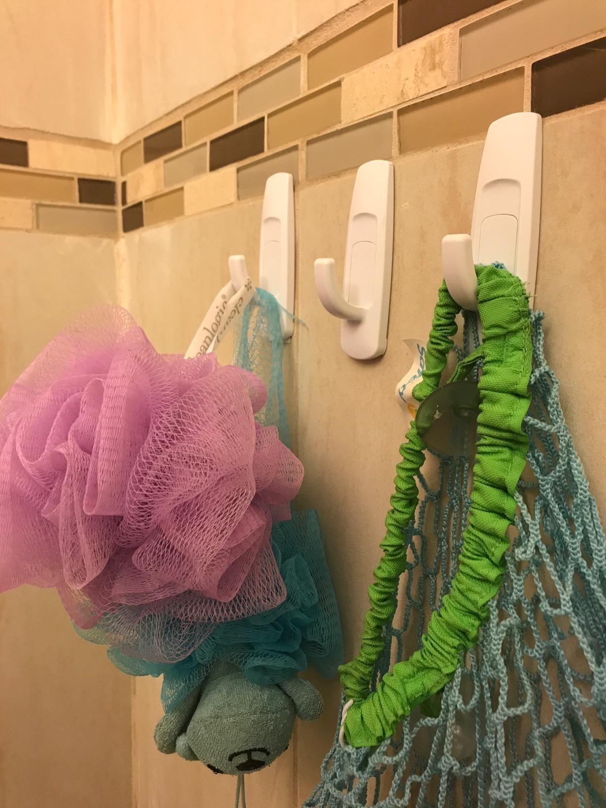 reviewer&#x27;s tile bathroom with three hooks holding loofahs and shower bags
