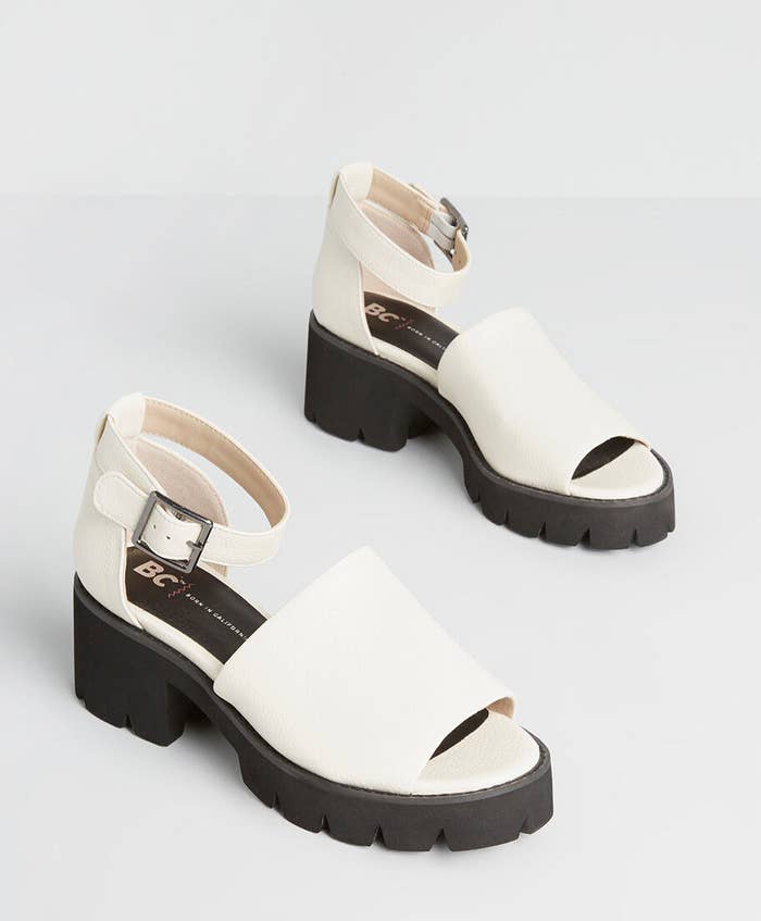 White sandals with chunky black soles, peak toes, and ankle straps with silver buckles