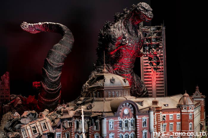 A replica of Godzilla destroys buildings under a reddish light