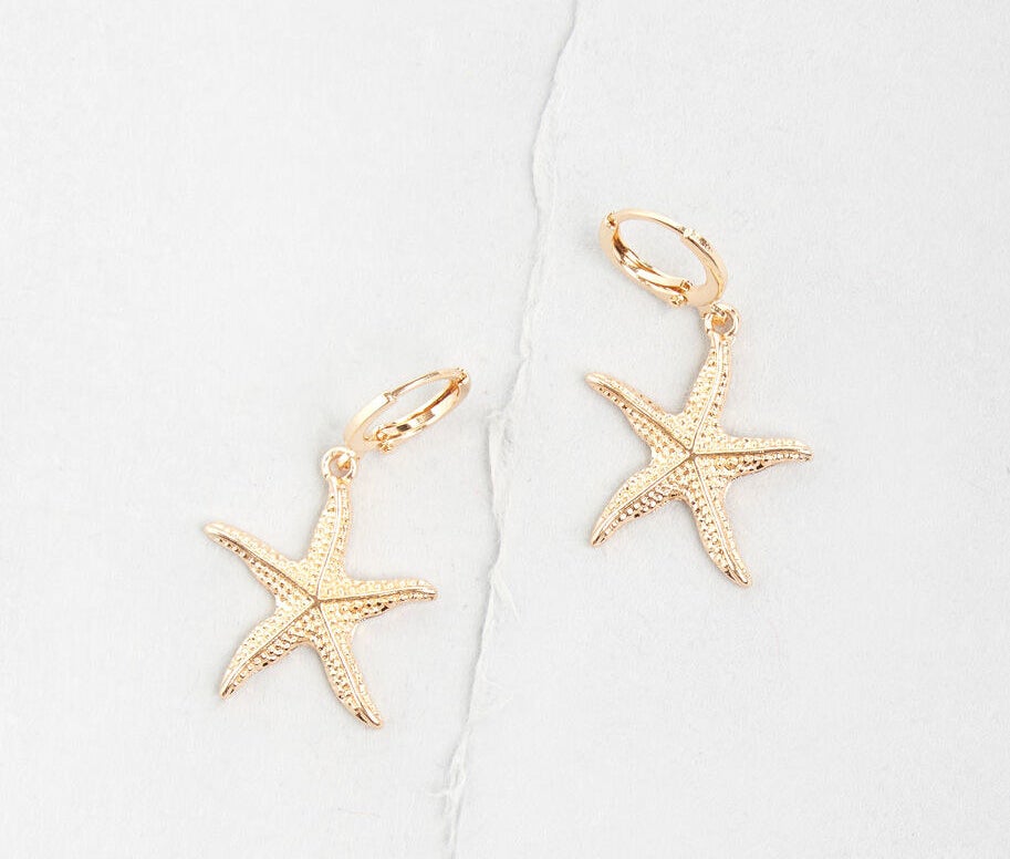 Two gold earrings with hoop clasps and dangling charms that look like speckled starfish