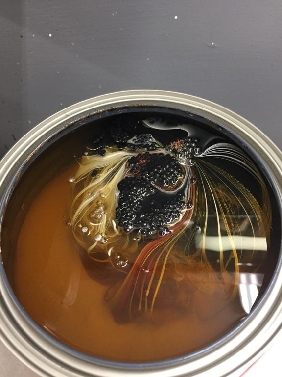 Unstirred paint has swirls of black, yellow, and red amongst cloudy orange