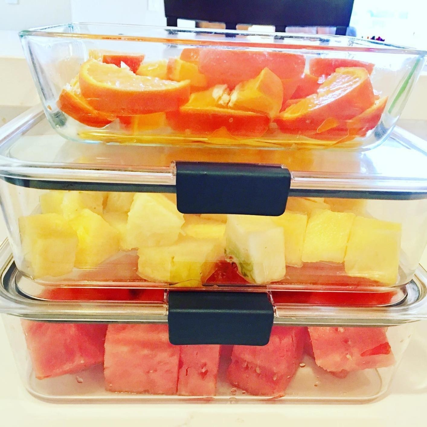 A reviewer showing slices watermelon, oranges, and pineapple inside three of the containers