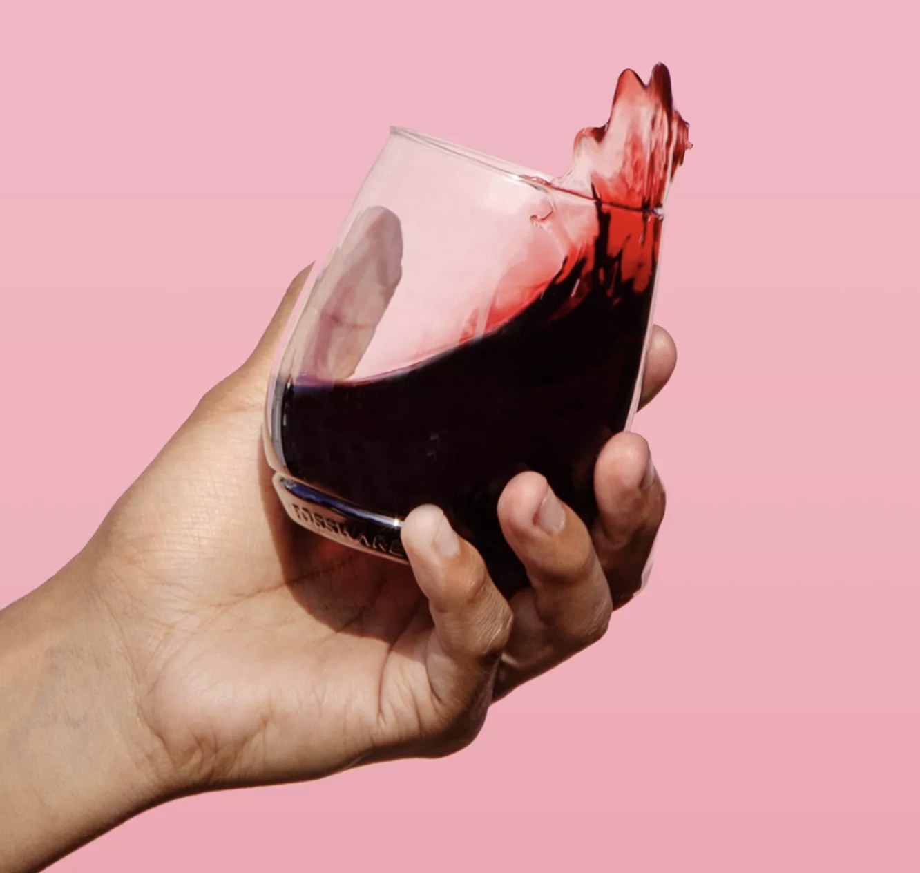 A hand holding red wine in the stemless glass