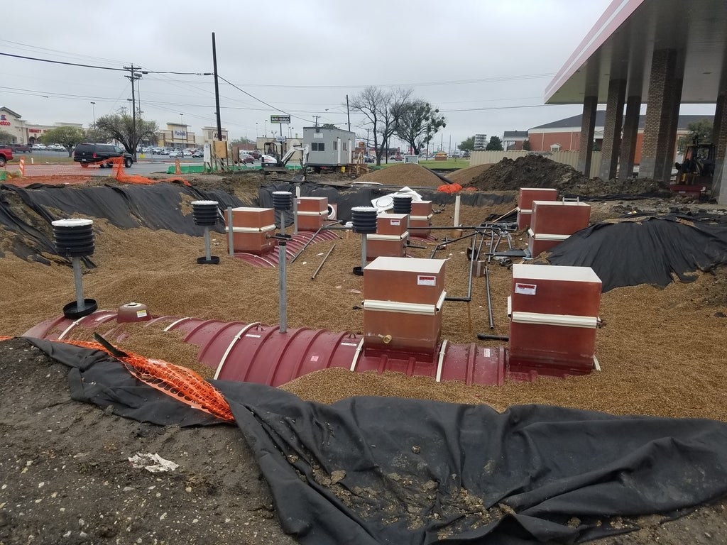 Large tanks and machinery covered in dirt are underground at a gas station