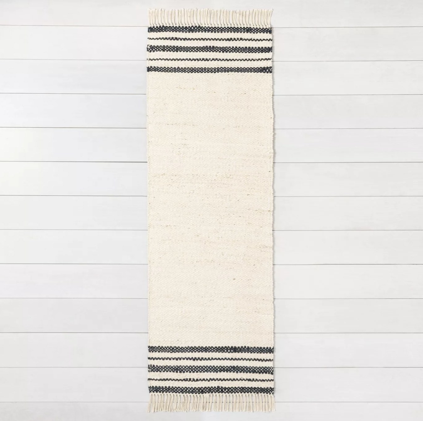 The narrow cream-colored rug with gray end stripes and frayed hems