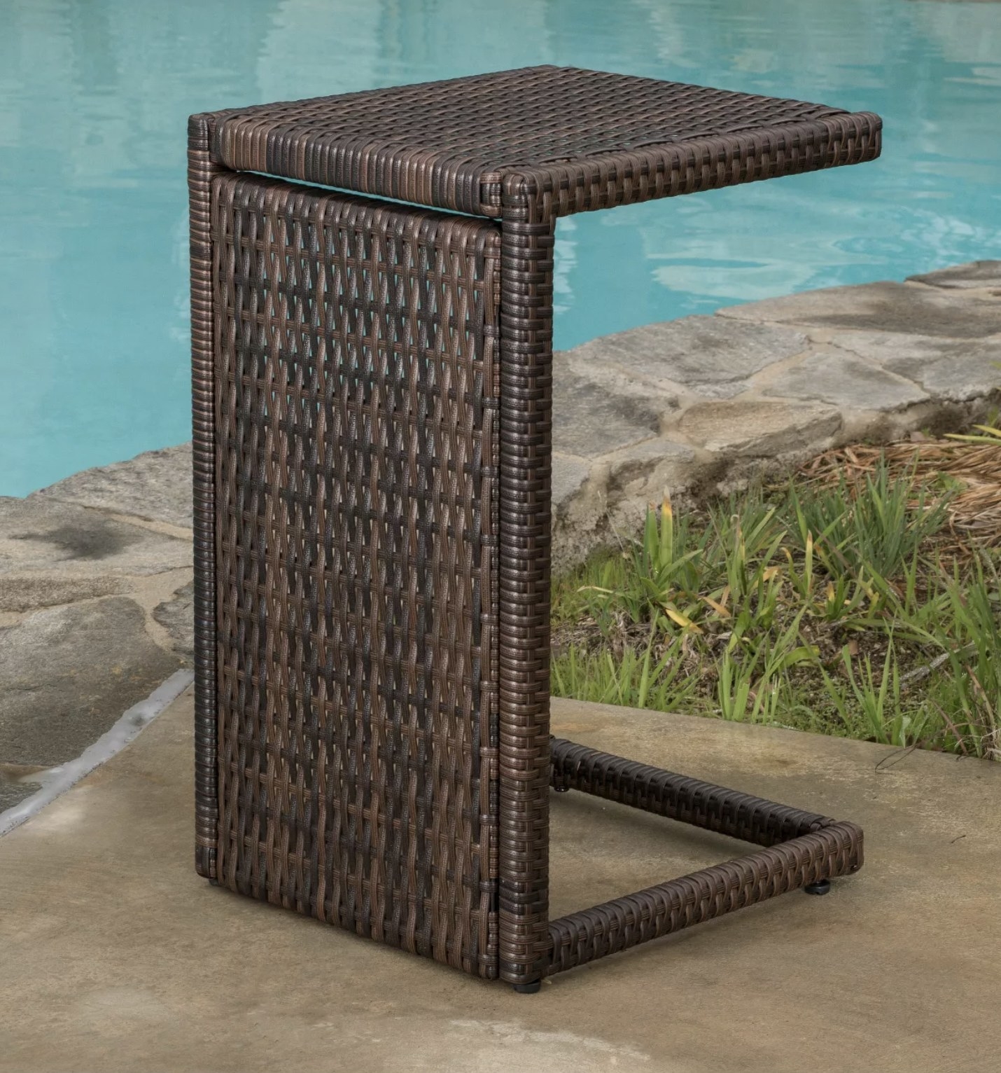A brown, wicker, c-shaped end table by a pool