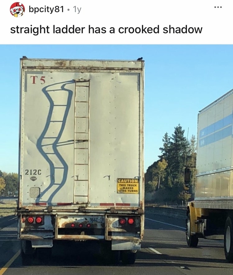 A semitrailer is driving down the road and the ladder on the back of it is casting a shadow that looks all wavy and bent