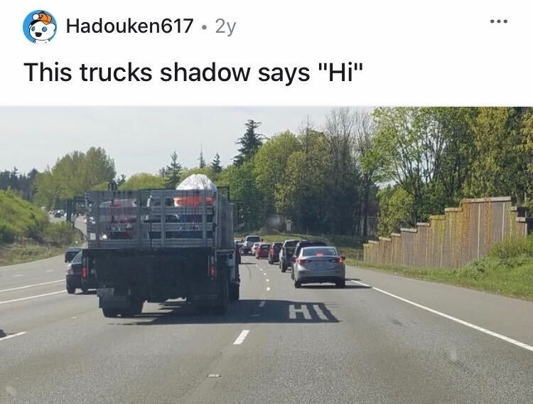 A truck is driving down the road and the bed of the truck is casting a shadow that says &quot;Hi&quot; on the road