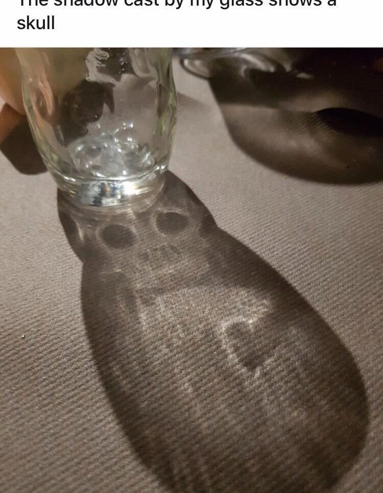 A glass is casting a shadow that has a creepy skull in it