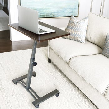 The adjustable desk with wheels at the bottom and brown wood top